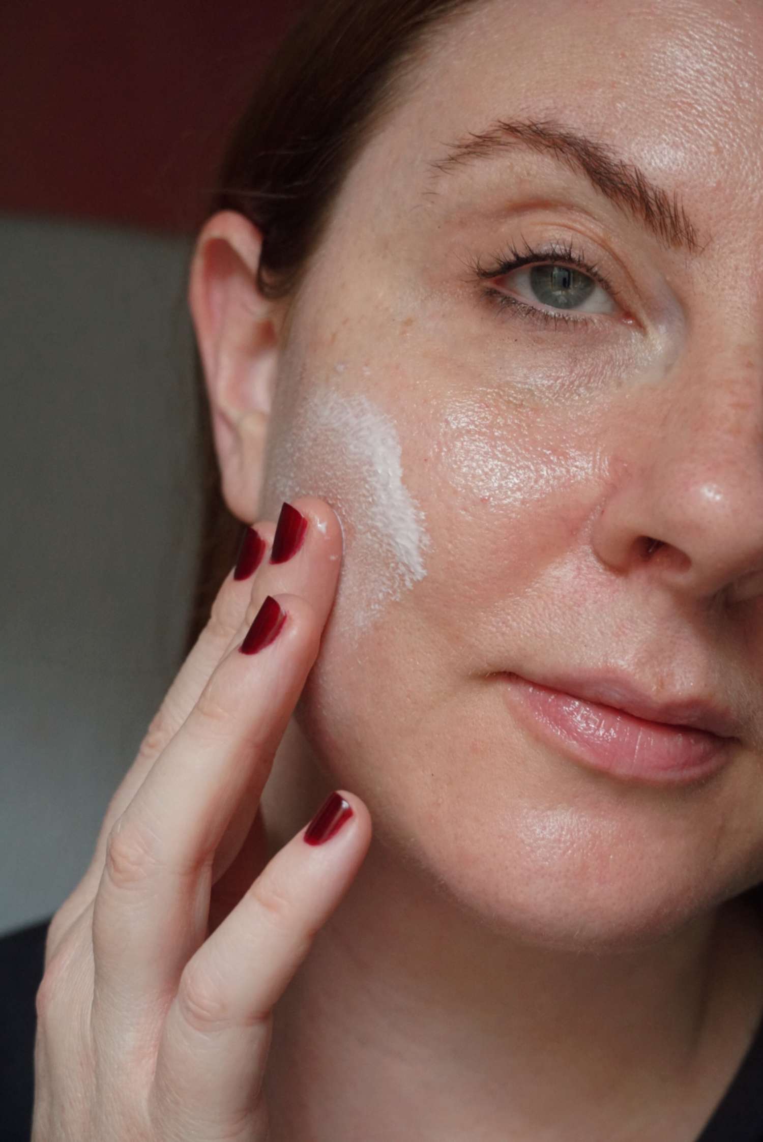 woman applying cream to her makeup-free face